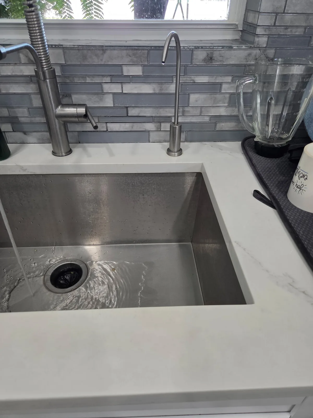Undermount stainless steel kitchen sink with modern faucet and gray tile backsplash
