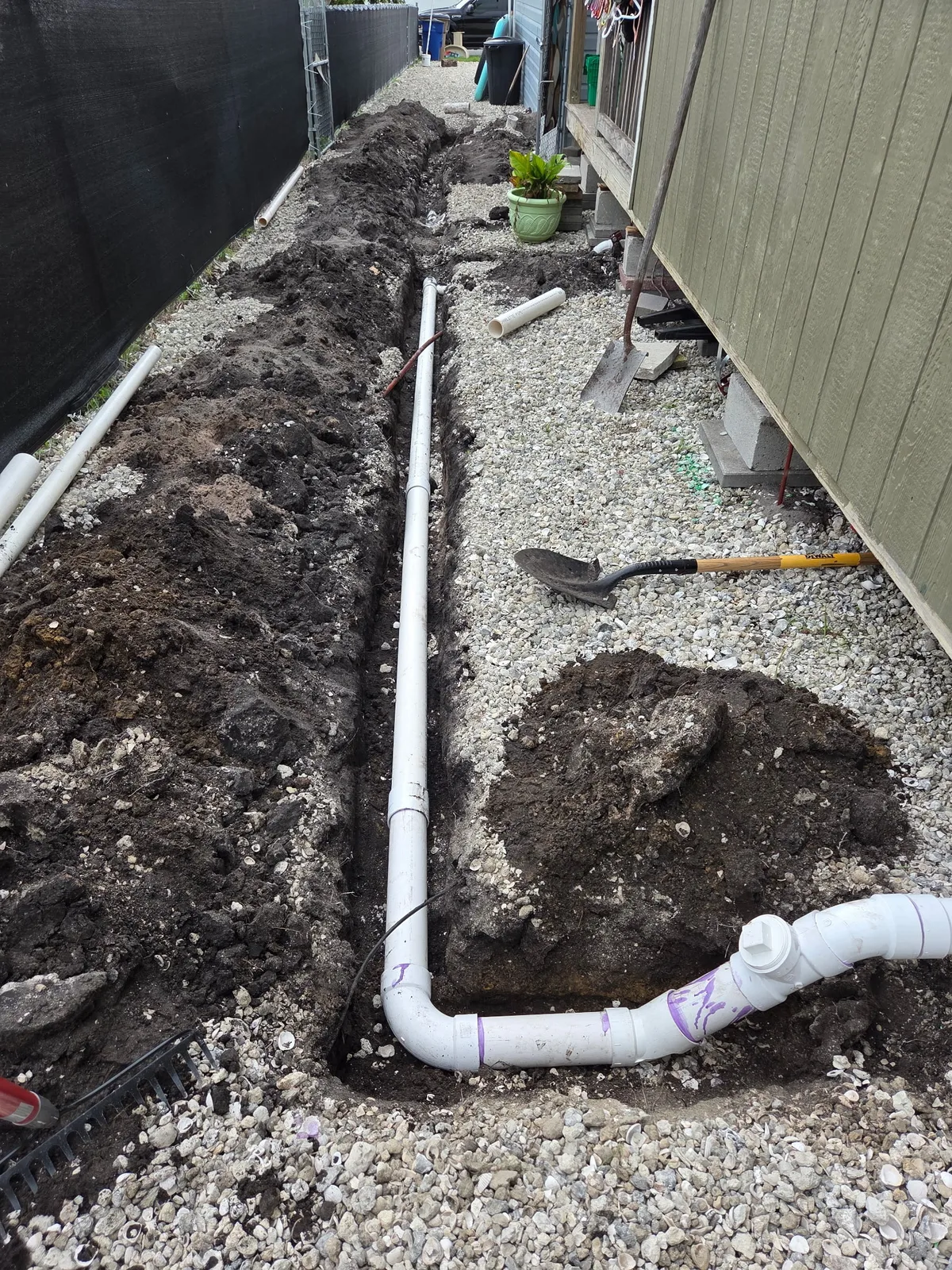 Open trench with new PVC piping running alongside a residential exterior wall