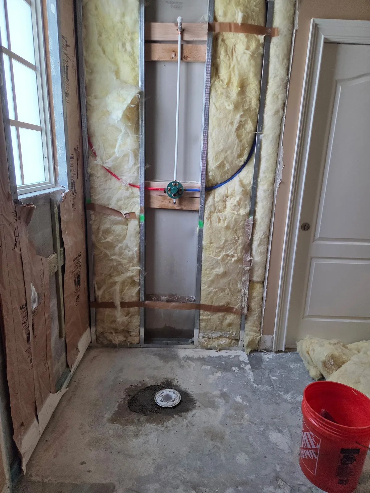 Bathroom rough-in plumbing at a doorway with red bucket on concrete floor