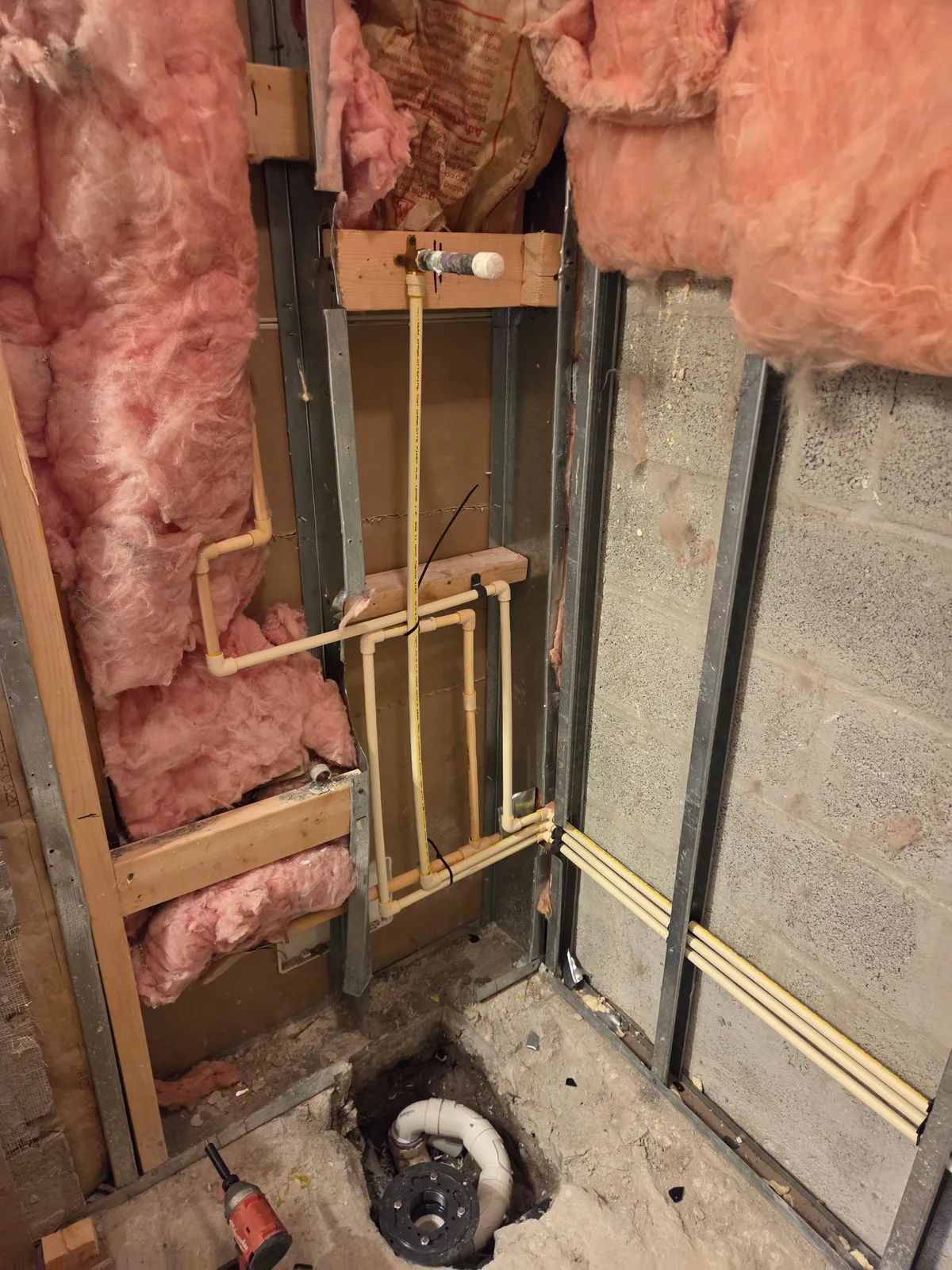 Rough-in copper and PEX plumbing lines inside an open wall cavity with insulation